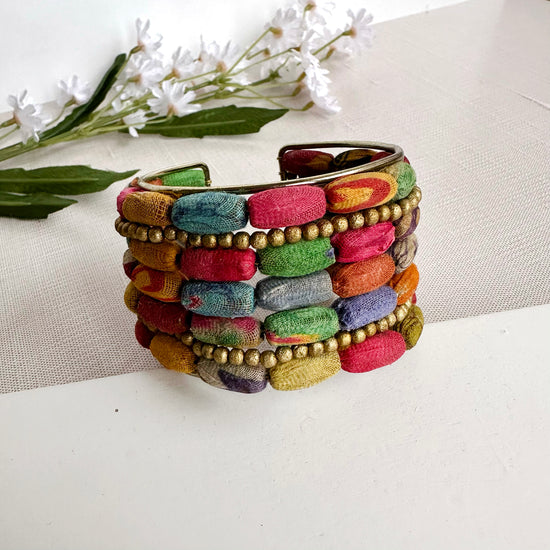 The front/top of a colorful multi-layered cuff is shown, propped up against a white board..