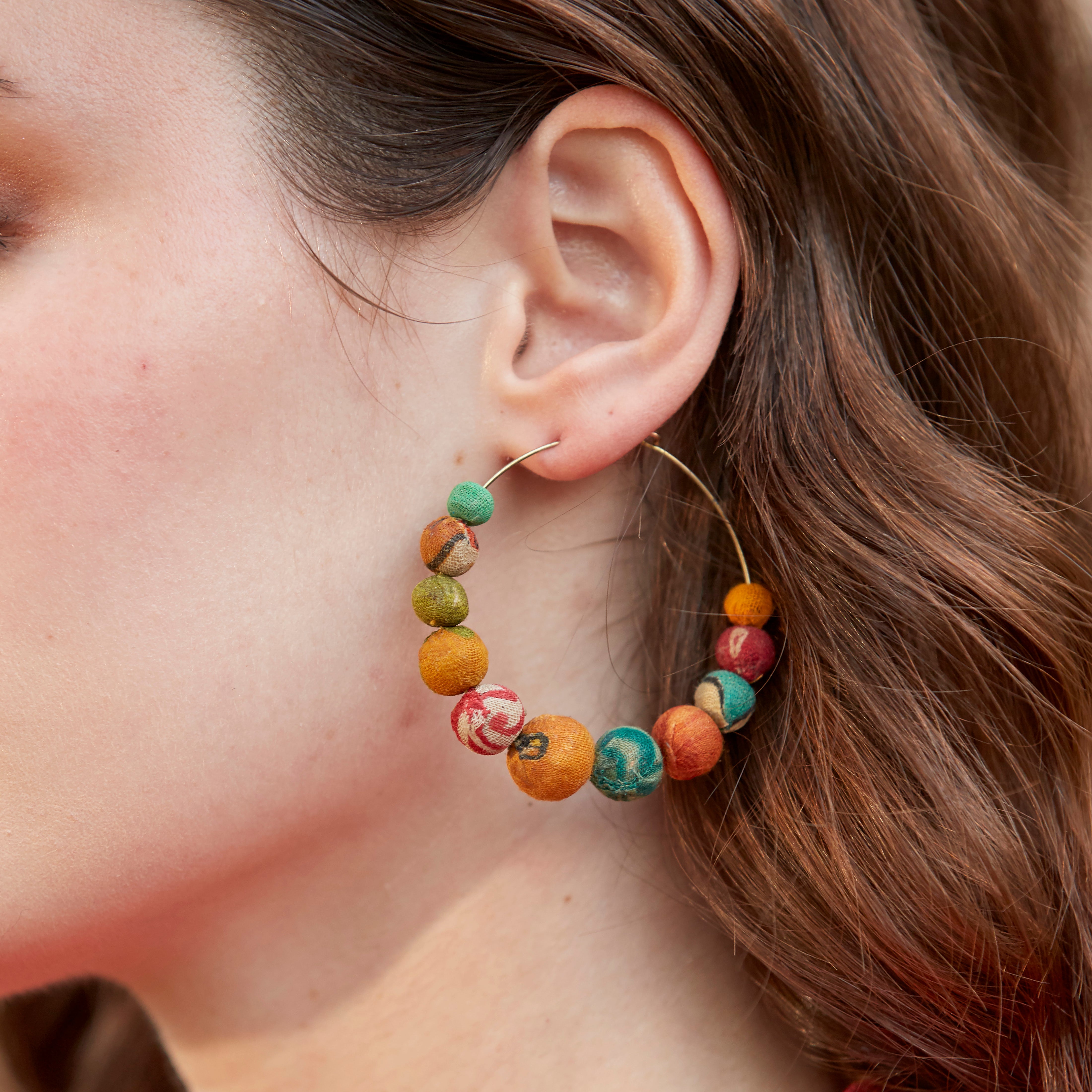 A woman wears the Kantha Graduated Hoops.