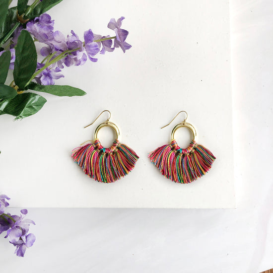 A pair of earrings is shown, each formed with six silky rainbow tassels fanning out from a metallic gold hoop.