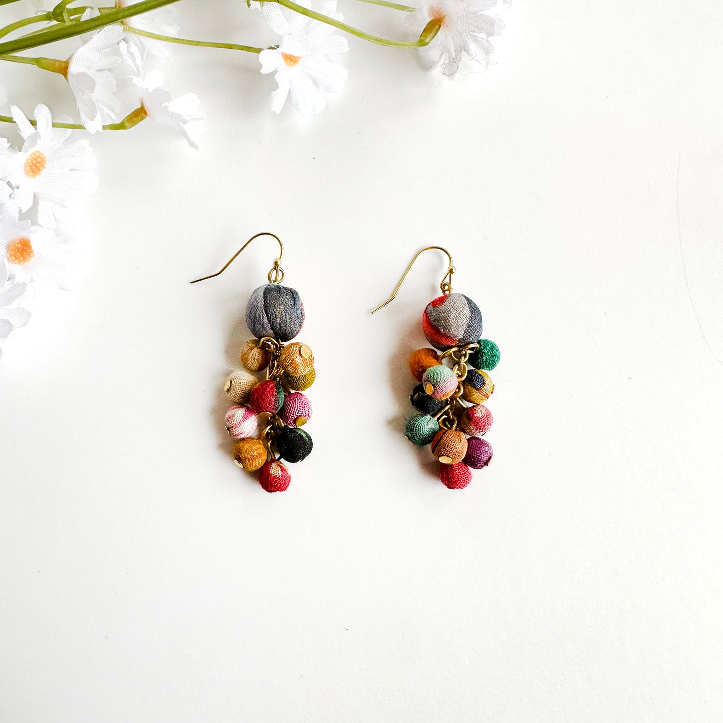 A pair of earrings is shown. A dangling cluster of multi-colored Kantha beads hang from a single statement bead on the top.