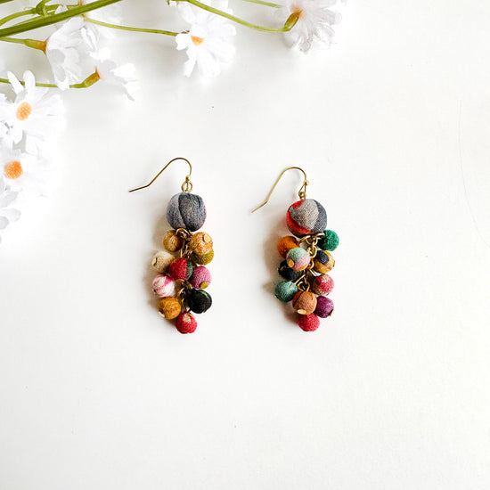 A pair of earrings is shown. A dangling cluster of multi-colored Kantha beads hang from a single statement bead on the top.