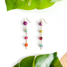 A pair of earrings is shown. A single Kantha bead is followed by a procession of 3 smaller beads, all at different points on a brass chain trail.