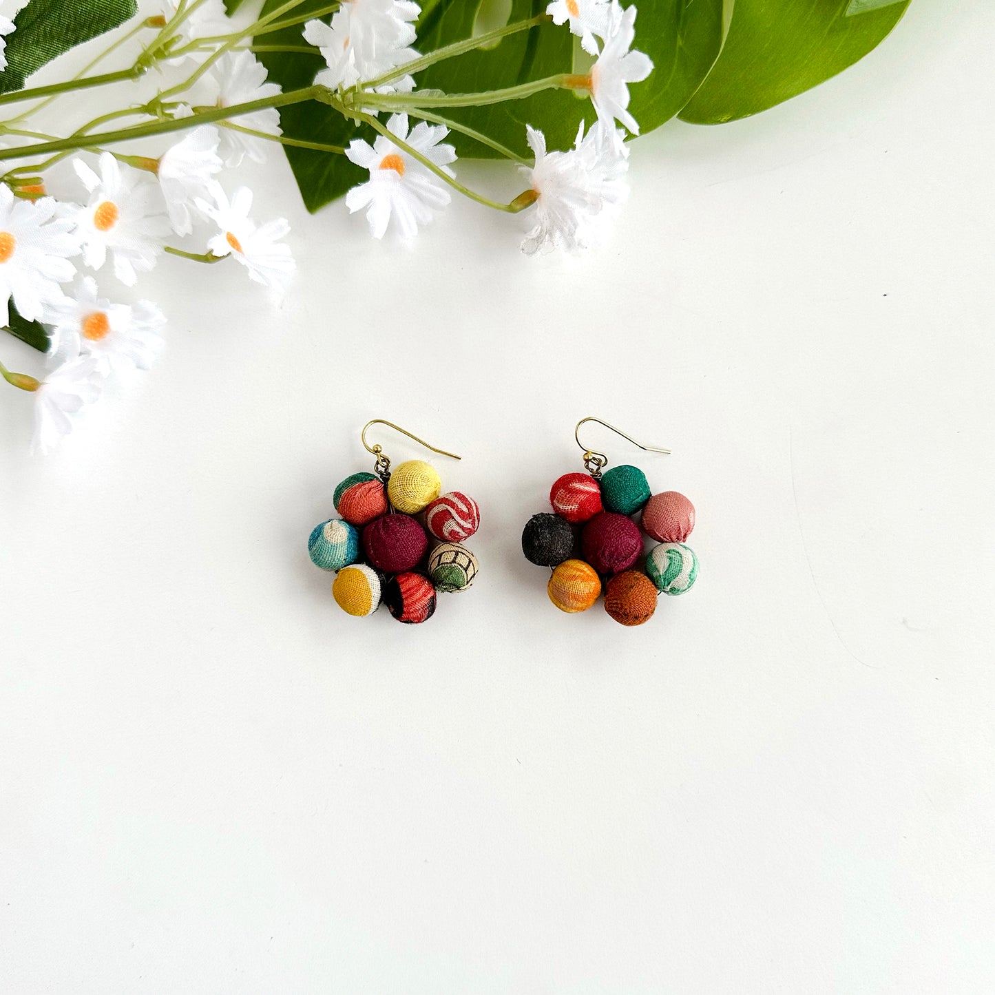 A pair of earrings is shown. These earrings are formed in the shape of a flower with a textile-wrapped bead in the center surrounded by seven smaller textile-wrapped beads acting as petals.