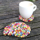 A stack of three multicolor Sari Home Circle Coasters sits on a wooden table.