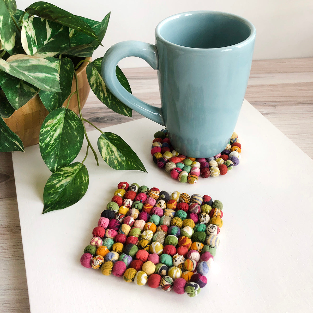 A blue mug rests on a Sari Home Circle Coaster with a Sari Home Square Coaster in the foreground.