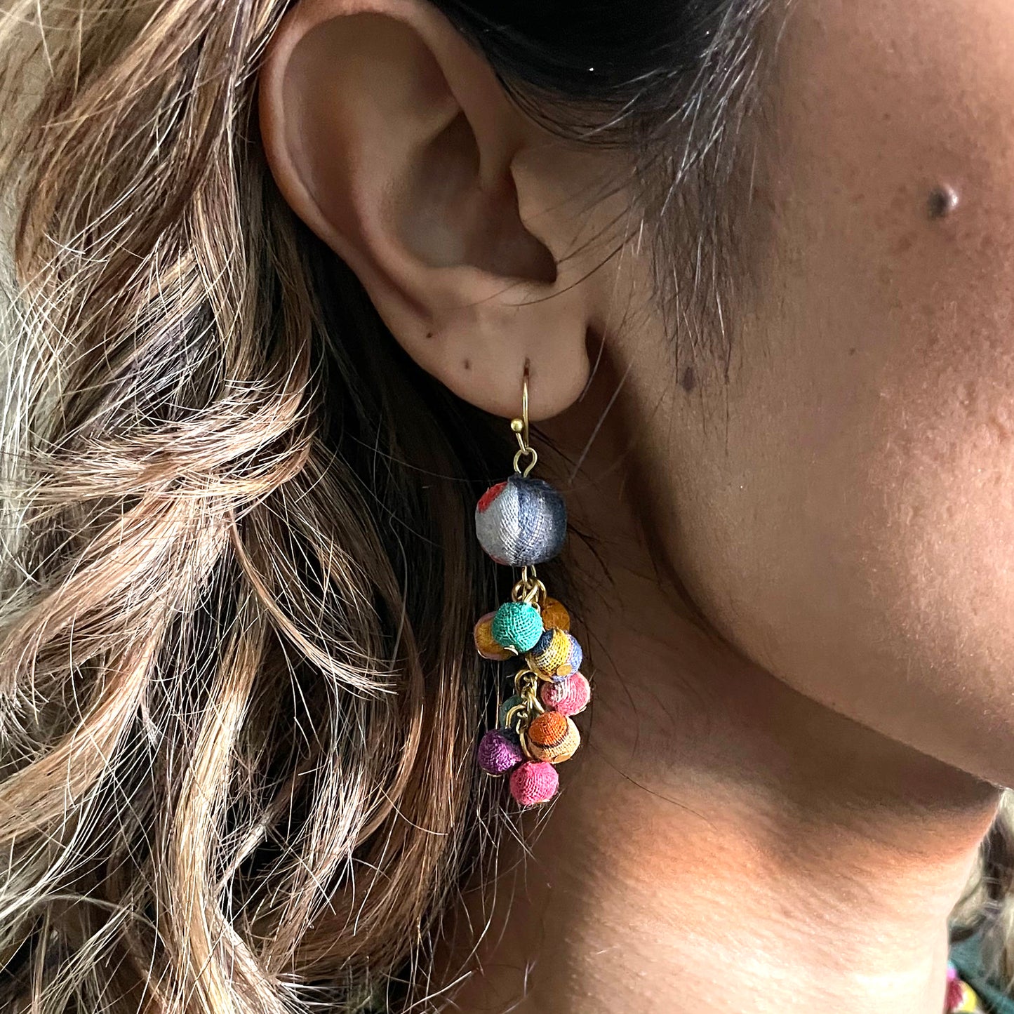 A woman's ear is shown modeling the Kantha Dangle Cluster Earrings.