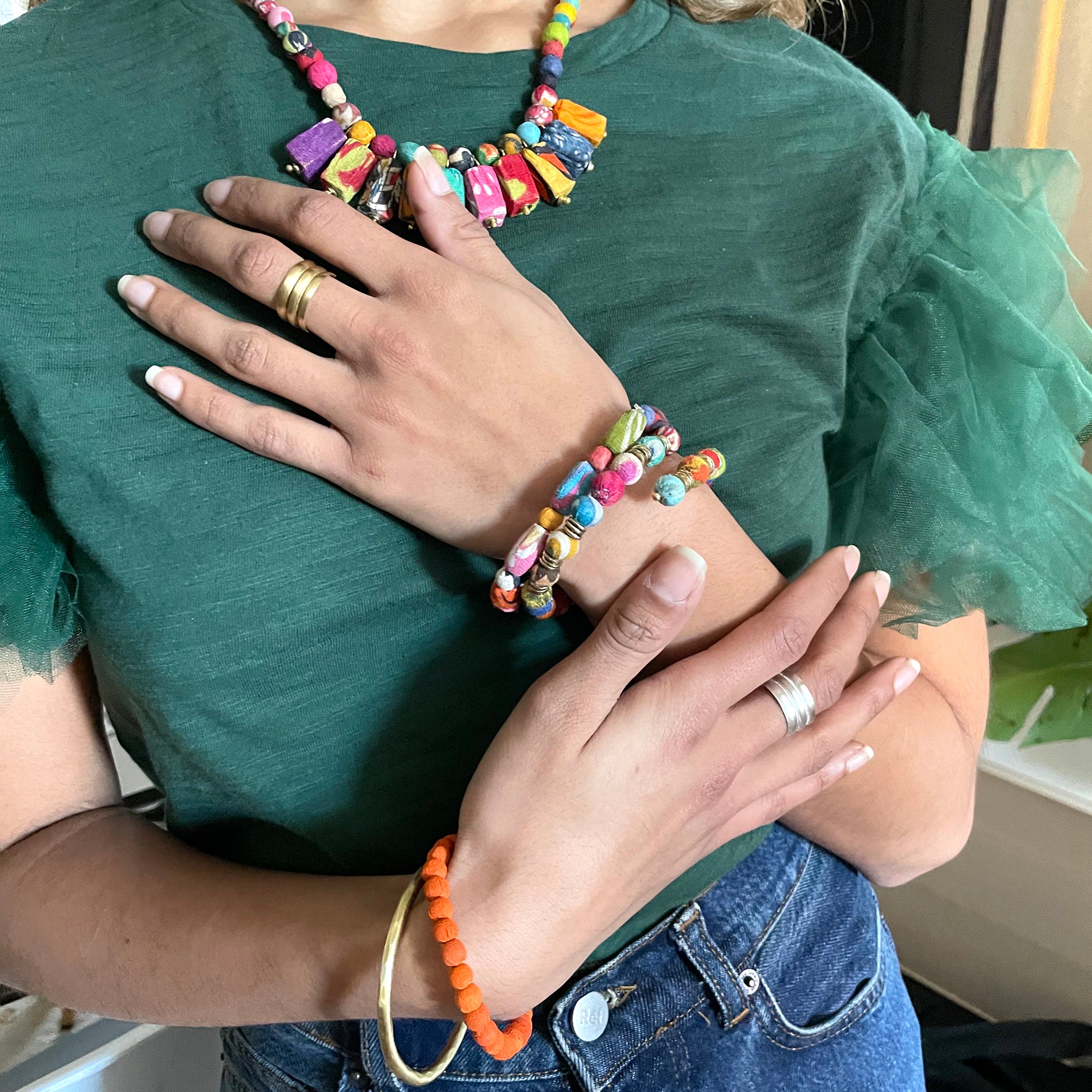 A woman places her hand on her chest, showcasing the bracelets on her wrist.