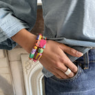 A woman's wrist, tucked into her pant's pocket, is adorned with two colorful bracelets.