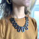 A close up of a black necklace is shown on a woman's neck.