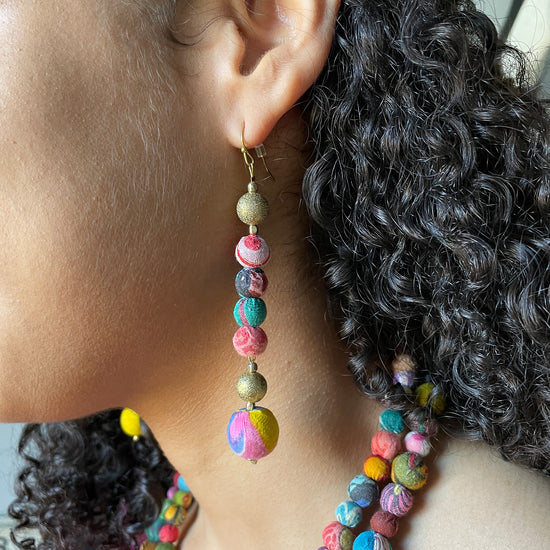 A woman's ear is shown wearing the Glimmering Kantha Linear Earrings.