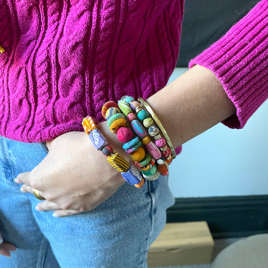 A woman's wrist, with her hand tucked into her pocket, showcases a stack of colorful textile-wrapped bracelets.