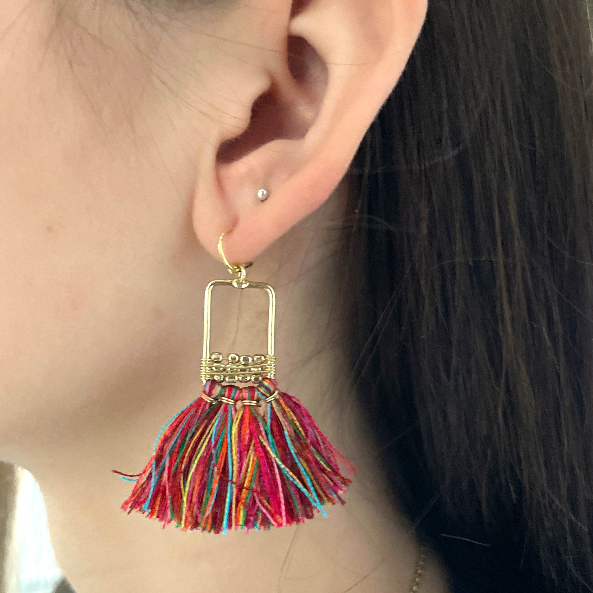 A woman's ear is shown with the Raja Linear Tassel Earrings.