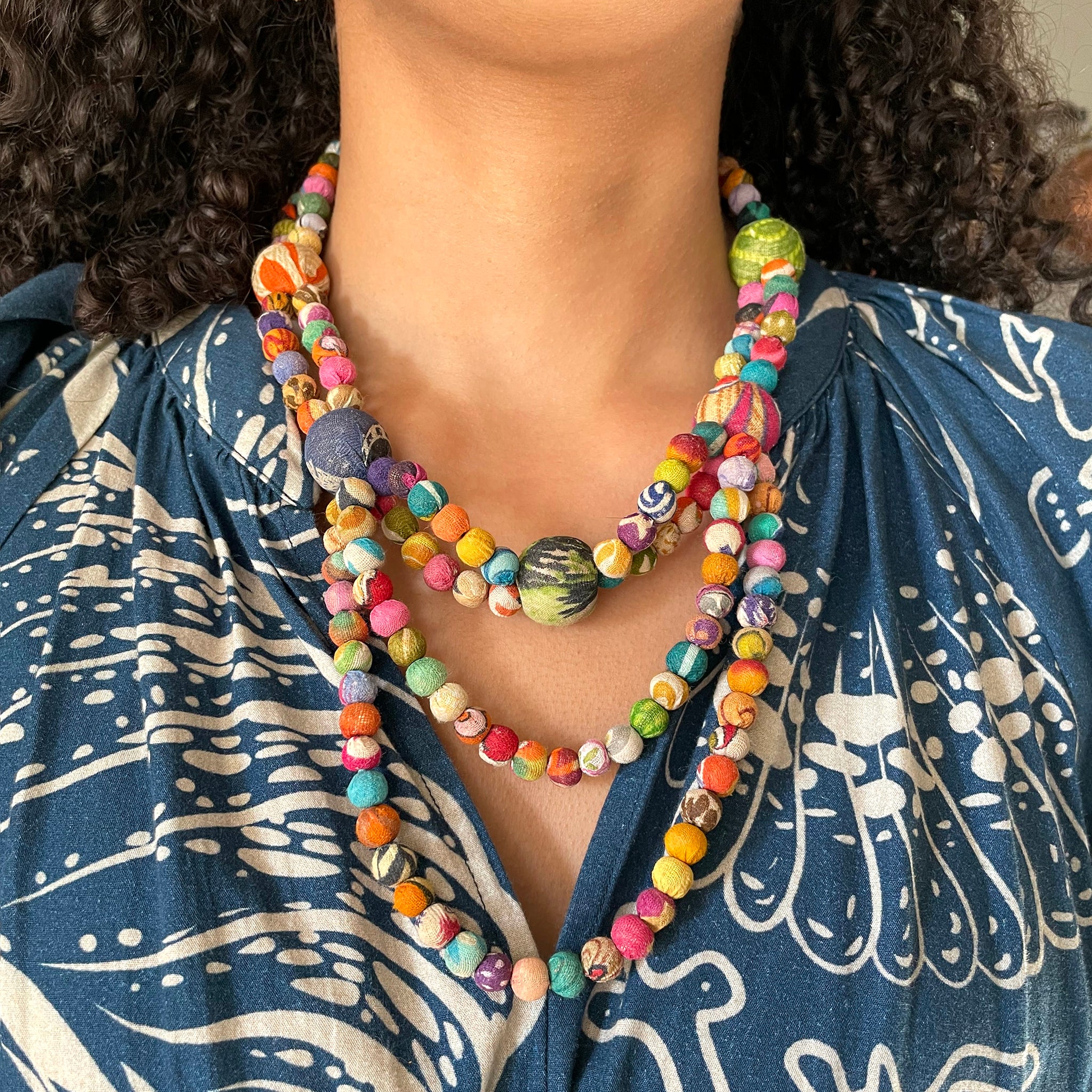 A close up of a woman's neckline shows a colorful necklace.