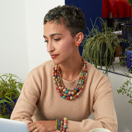A woman sits at a table while wearing the Kantha Aura Necklace.