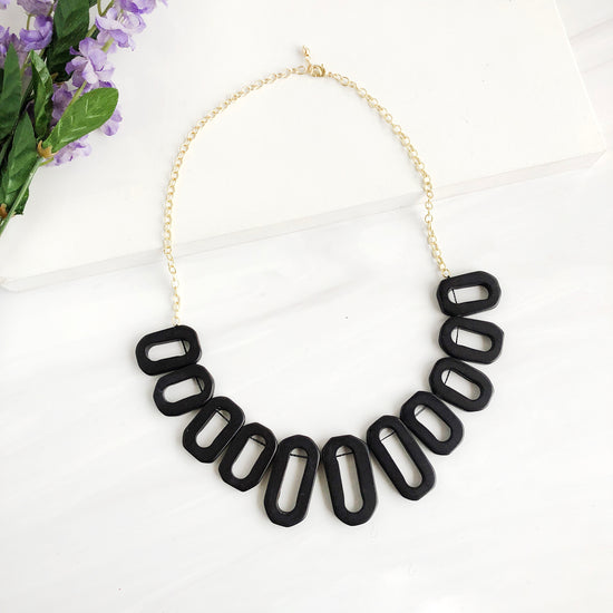 A necklace with black-toned geometric rectangle charms is shown against a white background.