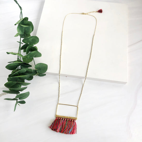 Rainbow hued tassels hang from a gold toned brass pendant, embellished with three rows of tiny brass beads.