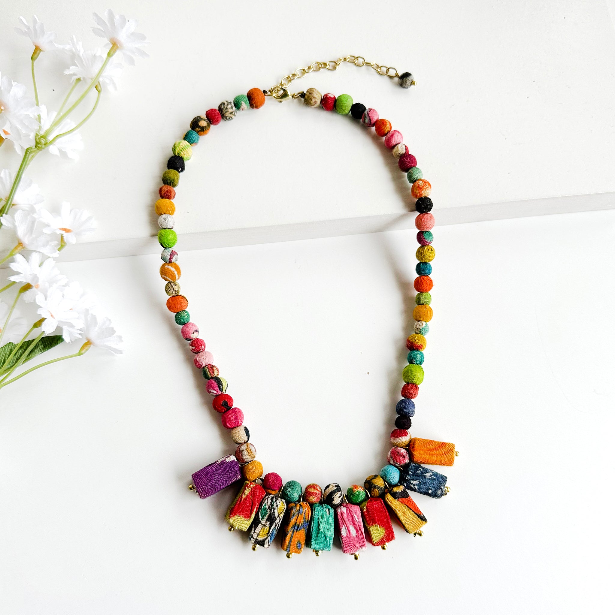 A colorful textile-wrapped beaded necklace features a fan of rectangular beads.