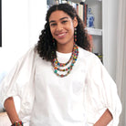 A woman smiles at us while modeling colorful beaded jewelry.