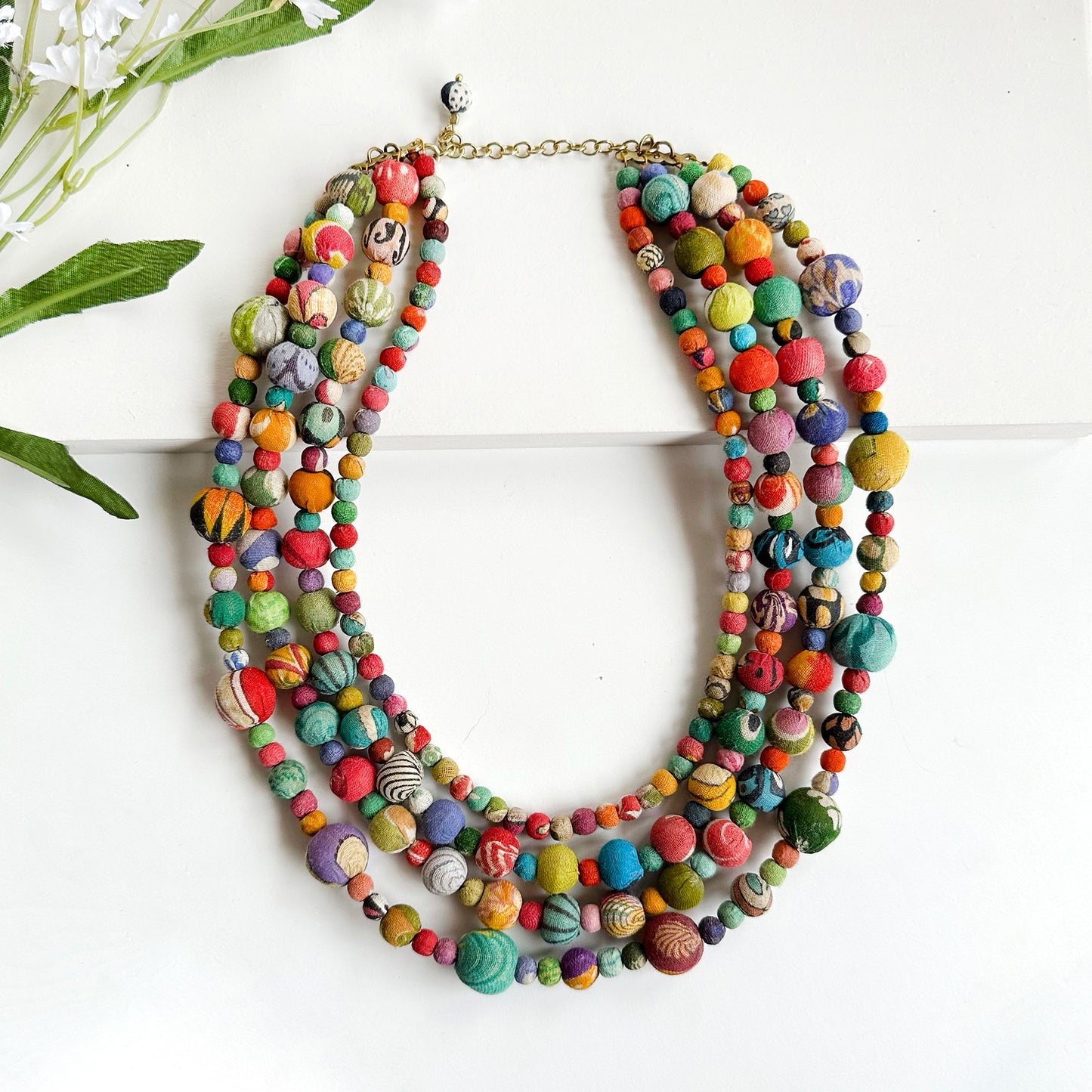 A colorful four-strand necklace features various alternating sized textile-wrapped beads.