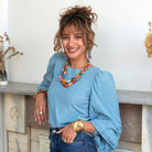 A woman smiles at us while modeling colorful beaded jewelry.