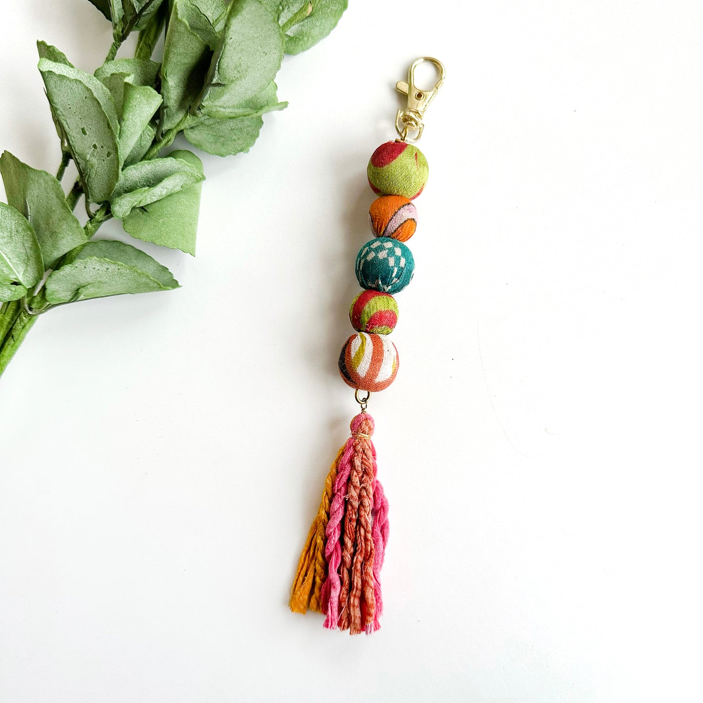 A keychain features five colorful textile-wrapped beads and is finished off with a colorful tassel.