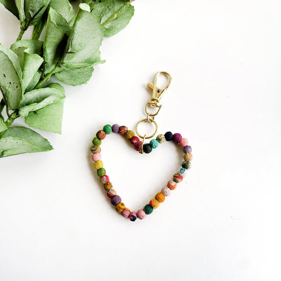 A heart formed from textile-wrapped beads is topped with a metal circle and lobster clasp.