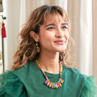 A woman smile away from the camera while modeling colorful beaded jewelry.