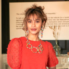 A woman smiles at us while modeling colorful beaded jewelry.