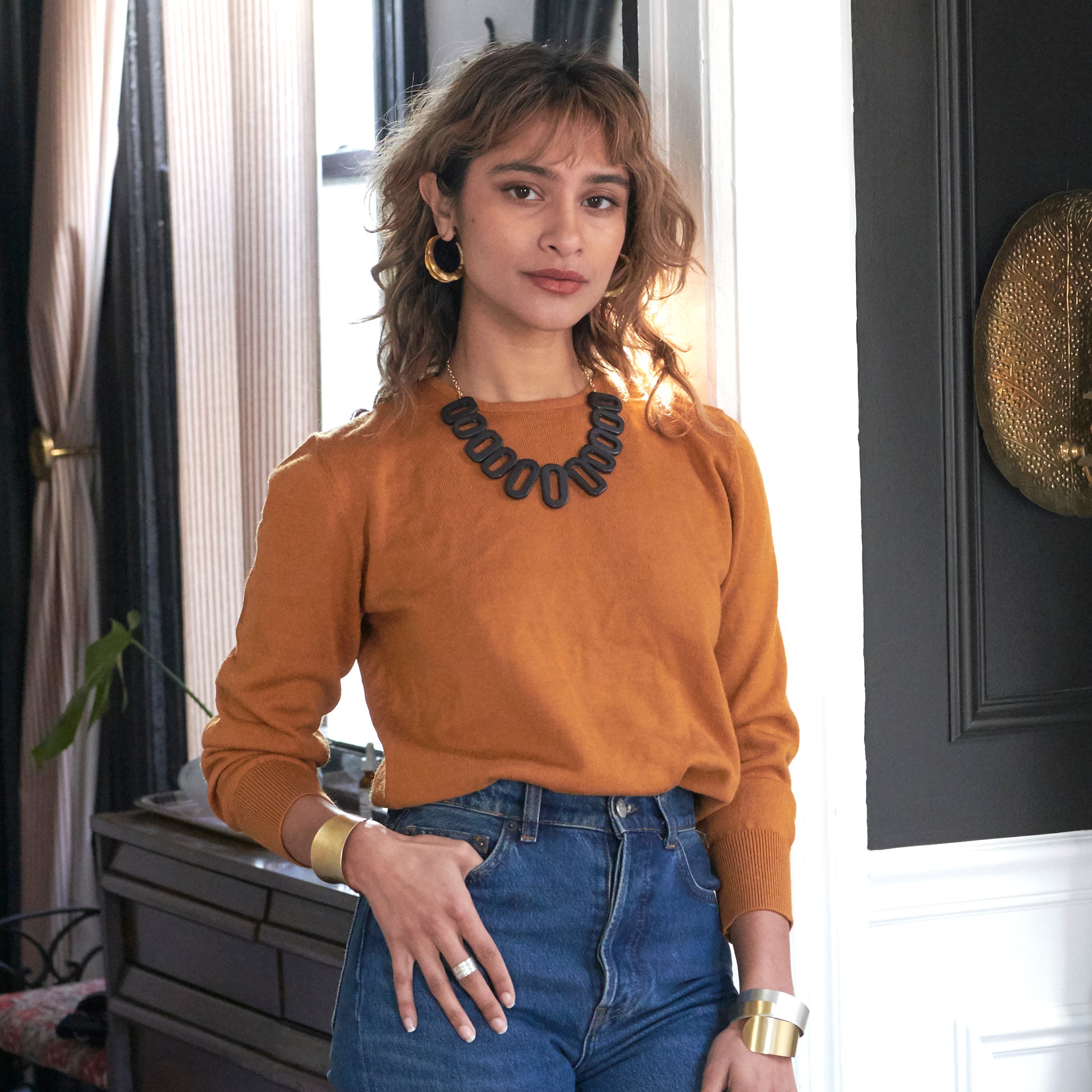 A woman looks at us while modeling gold and black jewelry.