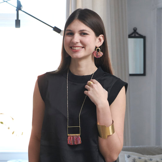 A woman smiles at us while modeling a collection of gold and rainbow-hued jewelry.