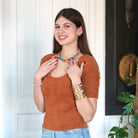 A model smiles while gesturing at her neckline and modeling the Classic Kantha Choker.