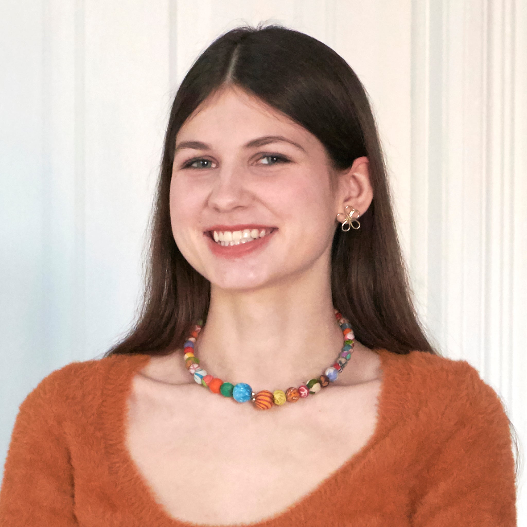 A woman smiles at us while modeling a colorful necklace.