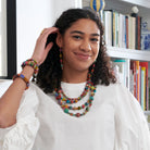 A woman smiles at us while modeling colorful beaded jewelry.