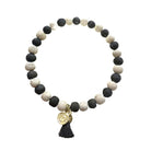 A black and white beaded bracelet with a black tassel and gold charm.