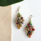 A pair of colorful, diamond-shaped earrings against a white background with a tan piece of fabric on the left.