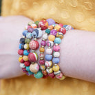 A close up of a woman's arm and then stack of six multicolor beaded bracelets.